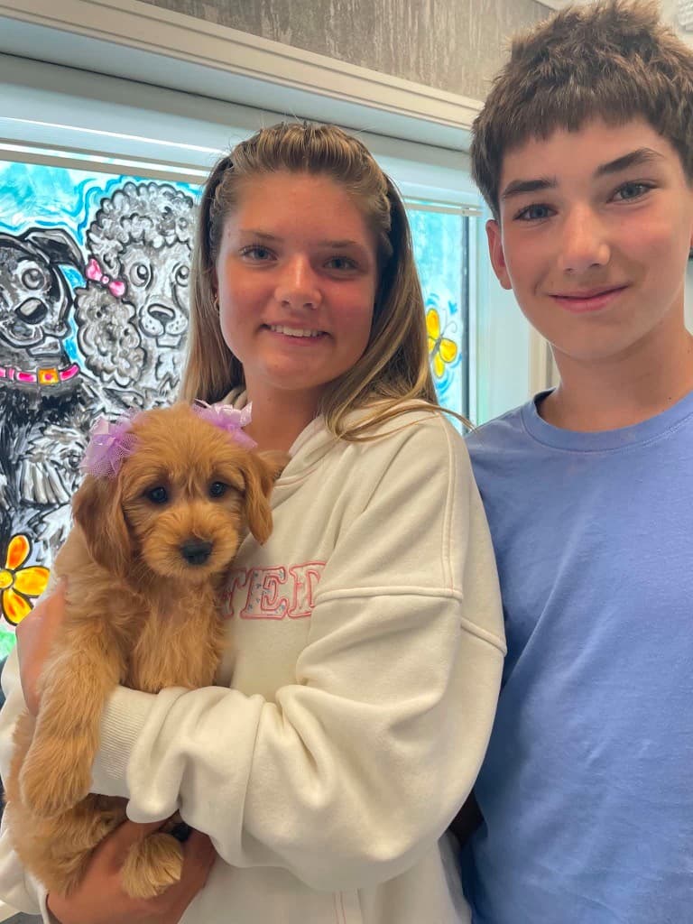 A brother and sister holding their new Goldendoodle puppy